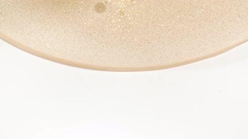Macro Shot of Transparent Yellow Cosmetic Fluid Gel Cream With Bubbles Flowing Down on a White