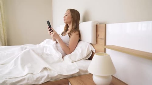 Woman Using Phone in Bed in Bright Room