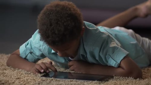Boy Uses Tablet on Carpeted Floor Indoors