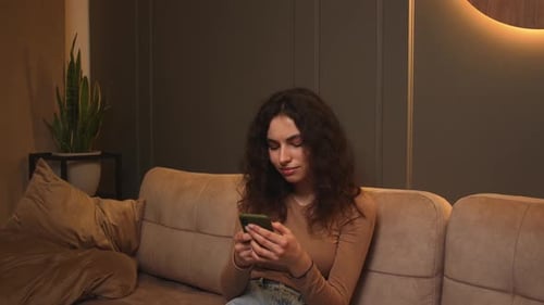 Woman Smiling and Using Phone on Couch