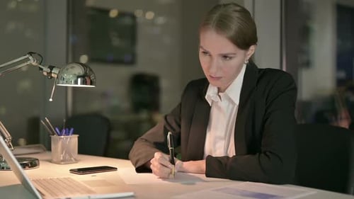 Woman Writing at Desk in Office at Night