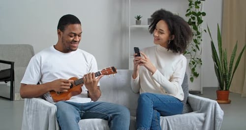 Man Plays Ukulele for Smiling Woman on Sofa