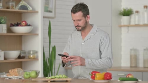 Man in Pajamas Using Phone in Kitchen