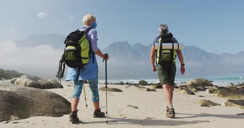 Rear view of senior hiker couple wearing face mask with backpacks and hiking poles
