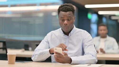 African Businessman Celebrating Success on Smartphone in Office