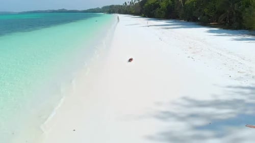 Aerial slow motion: Woman relaxing on white sand beach turquoise water tropical coastline