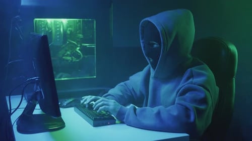 Hooded Hacker Typing on Computer Keyboard at Night