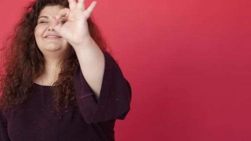 Smiling Woman Gestures Okay Sign on Red Background