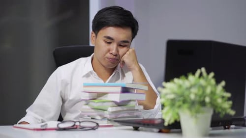 tired student sitting at the table with book and laptop
