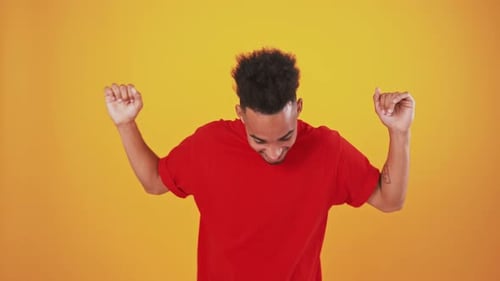 Happy African American Guy Dancing on Orange Studio Background Flirting to Camera