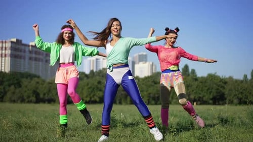 Front View Happy Slim Retro Sportswomen Exercising to Disco Music Outdoors in Sunshine