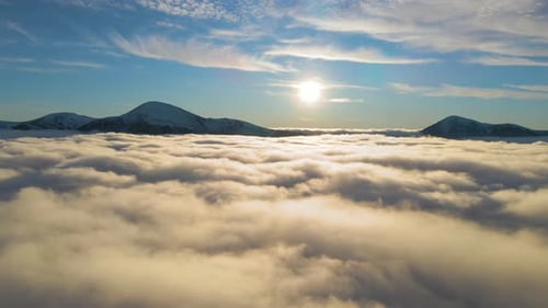 Aerial view of vibrant sunrise over white dense clouds with distant dark mountains on horizon.