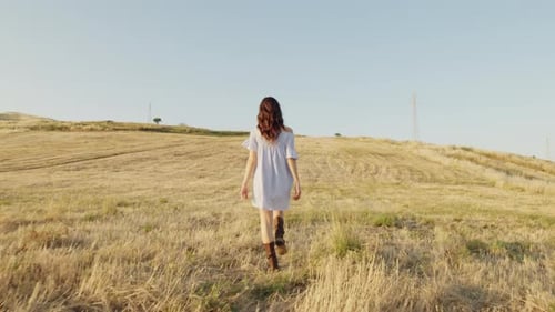 Woman Walking Through Golden Field on Sunny Day