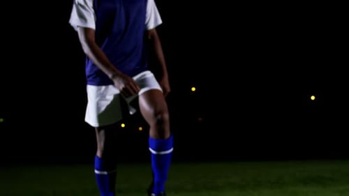 Soccer Player Kicking Ball on Field at Night