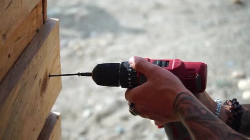 Hands of the Person with Electric Tool Unscrew the Selftapping Screw From a Wooden Board