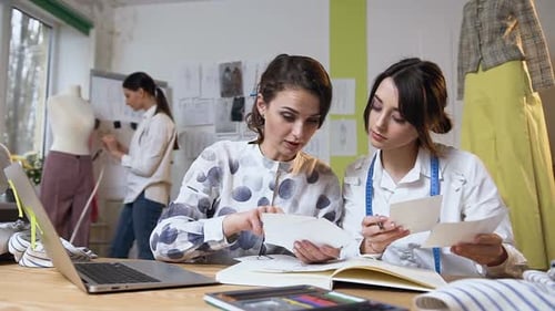 Two Female Tailors During Work with Sketches of Clothes