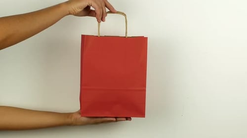 Arms Hold Red Paper Shopping Bag Against White Wall