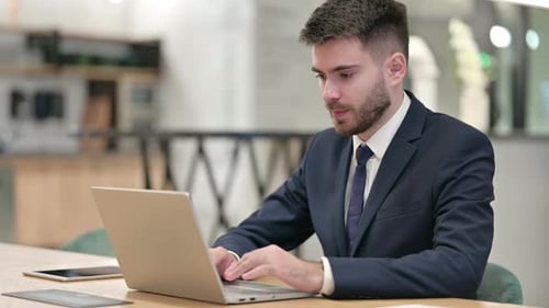 Excited Young Businessman Celebrating Success on Laptop in Office