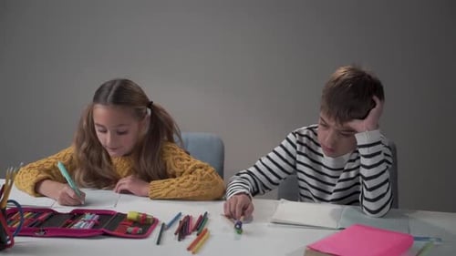 Sad Caucasian Boy and Happy Girl Sitting at the Table at School or at Home
