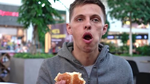 Close Up Shot of a Handsome Caucasian Male Eating a Burger in a Fast Food Restaurant