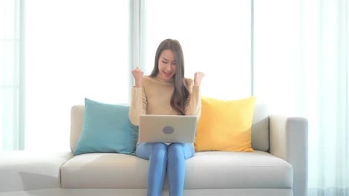 Young Woman on Laptop Celebrating Success on Couch
