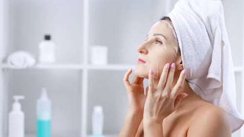 Woman with Facial Sheet Cosmetic Mask Makes Herself Facial Massage