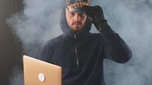 Hooded Man Holds Laptop with Halloween Mask