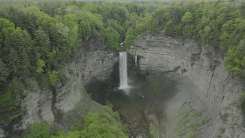 Drone shot, flying to the right, showing a big waterfall, in a canyon with trees surrounding it.