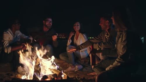 Friends Gather Around Campfire at Night, Play Guitar