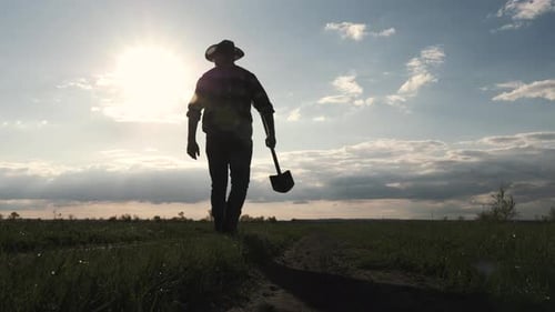 Farmer Walks With Shovel on a Rural Path