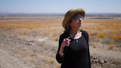 A happy middle aged woman with gray hair walking in a field of flowers on a hike with her walking st