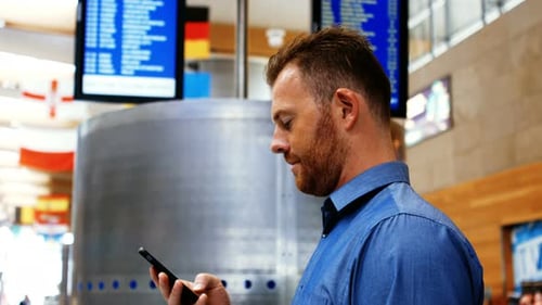 Man using mobile while looking at flight information display system
