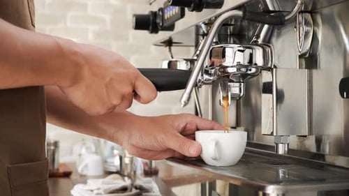 Barista holding cup getting fresh coffee that being brewed by the machine in cafe - dolly shot