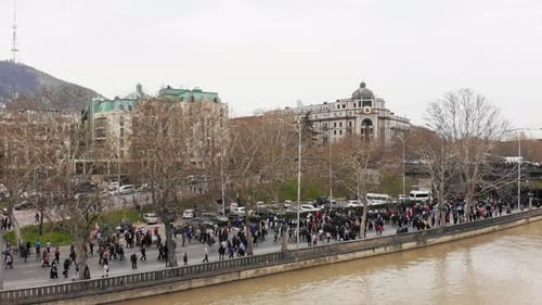 Crowd of People Walking Along City River Embankment