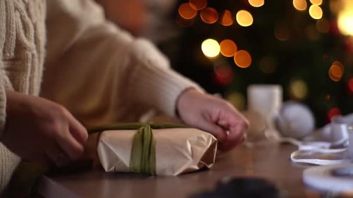 Woman Wrapping Christmas Present with Ribbon at Home