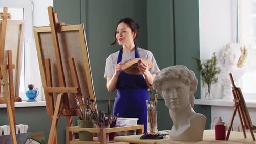 Pretty and Smiling Woman Works with a Painting on Easel in the Art Studio