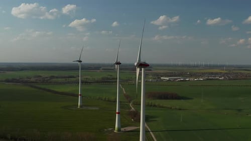 Seitenansicht einer Gruppe von Windkraftanlagen auf Türmen hoch über der grünen Wiese