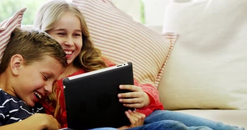 Children Laughing at Tablet on Couch Together