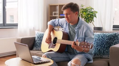 Young Adult Playing Guitar at Home with Laptop