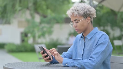 Young African Woman Using Smartphone in Outdoor Cafe