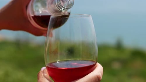 Eine Frau gießt Wein in ein rotes Glas. Weintrinkglas in Nahaufnahme in den Händen.