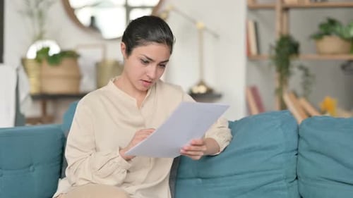 Woman Reviews Documents at Home on Sofa