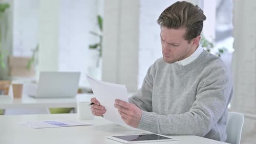 Kreativer junger Mann überprüft Finanzdokumente, liest