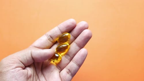 Fish Oil Supplement on Hand on Orange Background