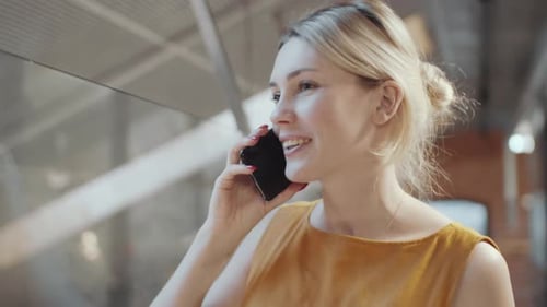 Blonde Businesswoman Talking on Mobile Phone beside Glass Wall in Office