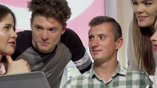 Young Adults Gather around Laptop in Bright Workplace