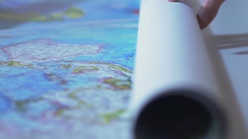 Man rollt die Weltkarte auf dem Tisch ab, touristische Planungsroute für Urlaub im Ausland