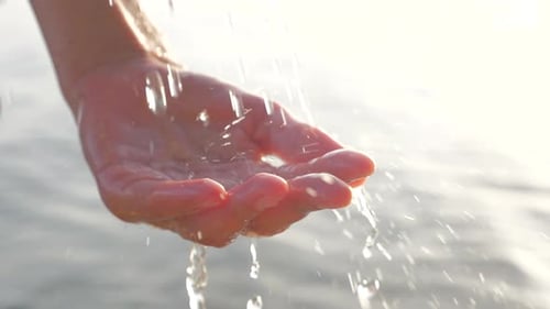 Woman Hand Playing with Drink Water Drops on Seascape Background