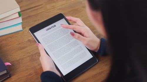 Female college student concentrating on reading e-book from tablet computer at the table