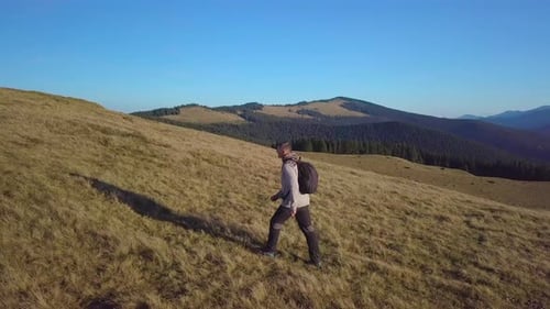 Man Hiking Across Grassy Hillside in Mountain Landscape